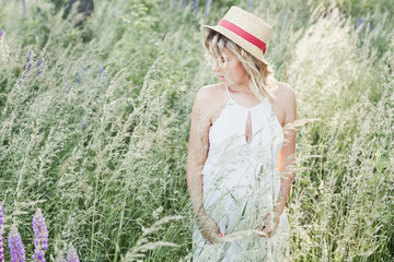 a beautiful pregnant woman with narrow margins hat stands among greenery lawn