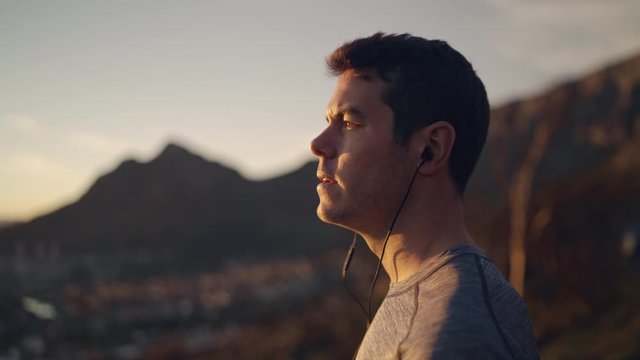 Side view of a fitness man listening to music using earphones overlooking at the cityscape view in early morning - admiring nature