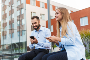 Obraz premium Colleagues man and woman businesspeople sit outside at the street using mobile phones.