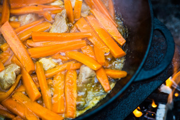 Roasted carrots with onions and meat in a cauldron. The process of cooking pilaf on the fire. Firefood