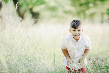 a little boy stands and smiles among greenery lawn