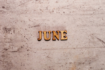 The word June laid out in wooden letters on a light background. Close-up. Summer time years and months of the year.