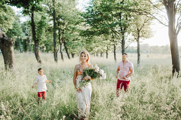 a woman holds a peony bouquet and a father with a son stand on the sides