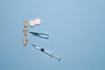The abbreviation IVF is laid out in wooden letters on a blue background. In vitro injection pen, tablet and ampoule. A syringe with a thin huge. IVF concept. Medication with hormones. Infertility.