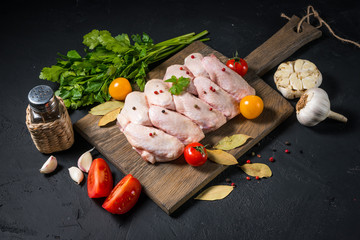 Raw chicken wings on a wooden board on a black background