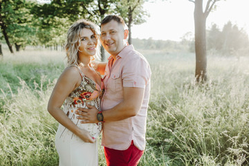  a portrait a man with her pregnant wife among greenery lawn