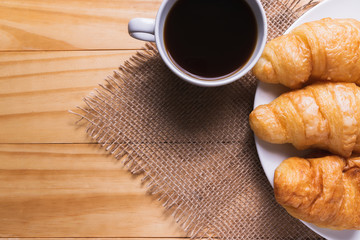 Closeup croissant with coffee on wooden table. breakfast concept.