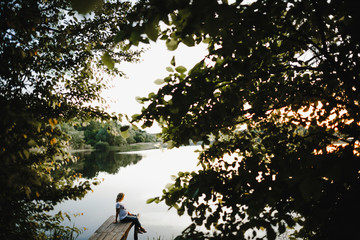 a pregnant woman sits on a bridge and looks at a lake