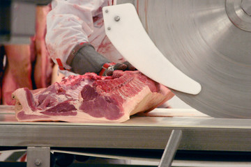 Portion of meat in a slaughterhouse. The butcher cuts meat on an industrial slicer