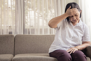 Fototapeta premium old age, health problem, vision and people concept - close up of Asian senior woman sitting on sofa and having headache at home.She may had Headache Symptoms.She looks pain and sick