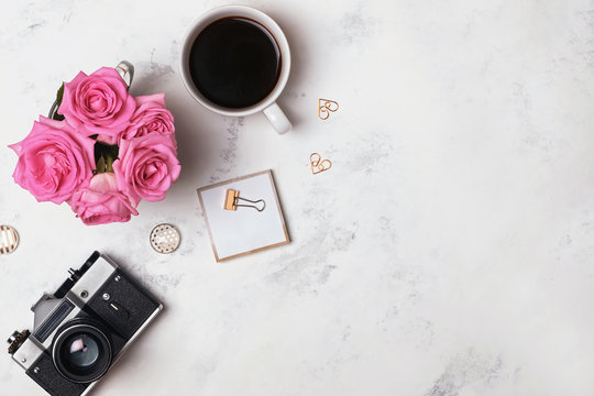 Coffee, roses, retro camera and gold stationery on the marble background