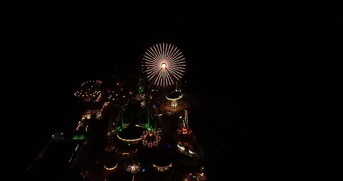 Boardwalk amusement pier aerial video footage from drone at night time bright lights against dark sky