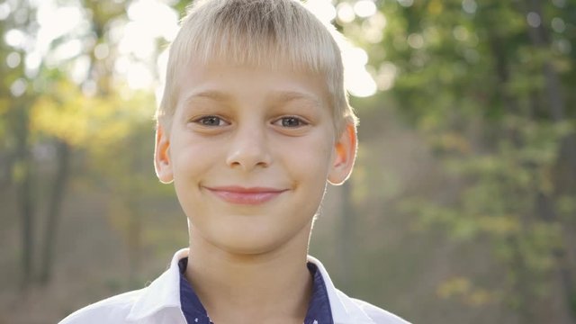 Close-up of a cute boy looking at the camera and smiling. Portrait of a child in the park in sun rays. Leisure activity, spending time outdoors.