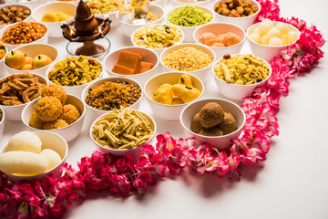 Rangoli of sweets and Farsan/snacks in bowls for Diwali with diya over white background