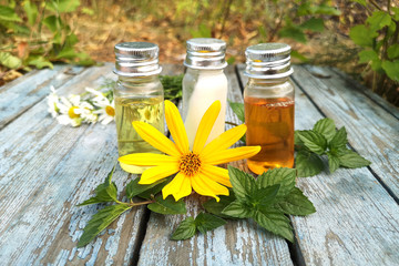 Cosmetic three bottles with white, yellow and orange body butter next to the yellow flower. The concept of 