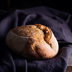 Freshly baked homemade sour dough bread on dark linen napkin, wooden background.