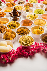 Rangoli of sweets and Farsan/snacks in bowls for Diwali with diya over white background