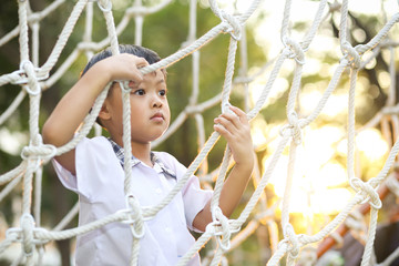 An Asian boy in school uniform playing alone at the rope net in the school playground.