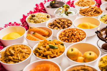 Rangoli of sweets and Farsan/snacks in bowls for Diwali with diya over white background