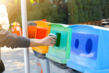 A man hand throwing a plastic glass into the green garbage bin.