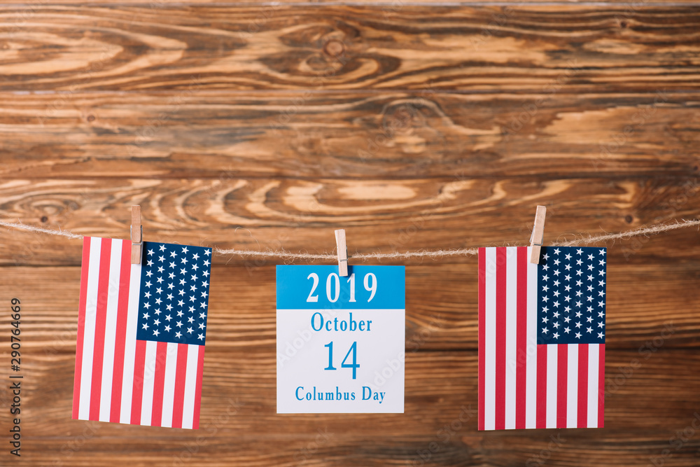 Sticker calendar with 14 October date between national flags of America on wooden surface