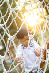 An Asian boy in school uniform playing alone at the rope net in the school playground.