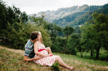 wait baby. happy family. pregnant woman with beloved husband sitting on grass, kissing. hand...