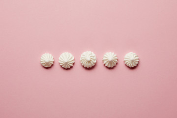 Flat lay with sweet white meringues in horizontal row on pink background
