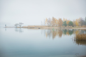 Fototapeta na wymiar Serene Scandinavian fall landscape of Southern Finland, Espoo in foggy day. Colorful autumn forest reflecting in calm sea water. Fallen leaves on water surface and misty sea. Serene Scandinavian fall 