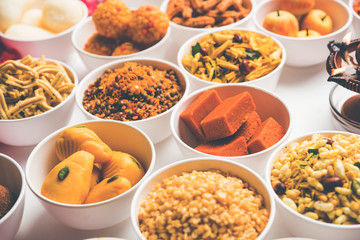 Rangoli of sweets and Farsan/snacks in bowls for Diwali with diya over white background