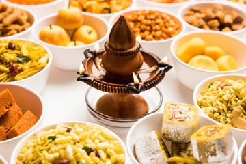 Rangoli of sweets and Farsan/snacks in bowls for Diwali with diya over white background