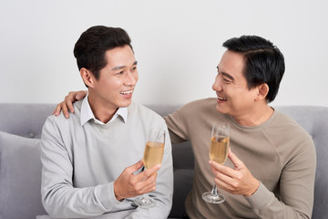 Happy friends men celebrating drinking sparkling wine and positive discussing while sitting on home sofa in apartment living room