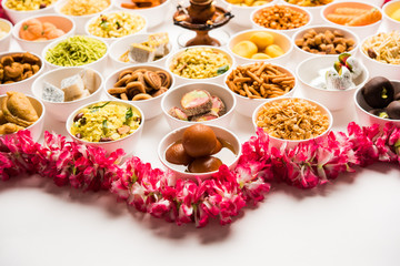 Rangoli of sweets and Farsan/snacks in bowls for Diwali with diya over white background