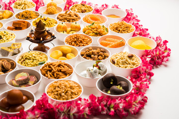 Fototapeta na wymiar Rangoli of sweets and Farsan/snacks in bowls for Diwali with diya over white background