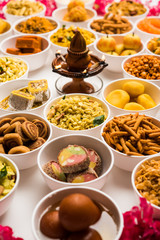 Rangoli of sweets and Farsan/snacks in bowls for Diwali with diya over white background