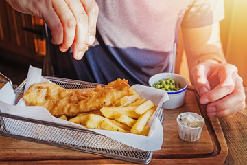 Man's hand sprinkling with lemon fresh delicious portion of fish and chips