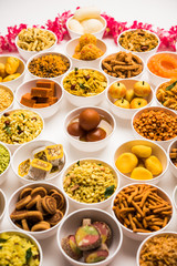 Rangoli of sweets and Farsan/snacks in bowls for Diwali with diya over white background