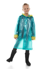 Full shot of a little blonde girl dressed in a green nacre raincoat, black jeans, black top and black high shammy boots. The raincoat with pockets is buttoned with press-studs,