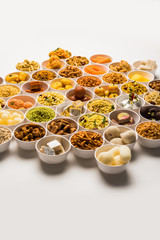 Obraz na płótnie Canvas Rangoli of sweets and Farsan/snacks in bowls for Diwali with diya over white background
