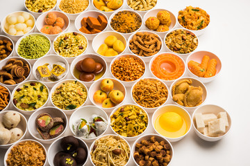Rangoli of sweets and Farsan/snacks in bowls for Diwali with diya over white background