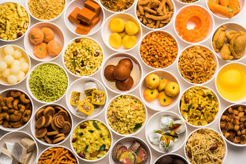 Rangoli of sweets and Farsan/snacks in bowls for Diwali with diya over white background