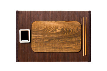 Empty rectangular brown wooden plate with chopsticks for sushi and soy sauce on dark bamboo mat background. Top view with copy space for you design