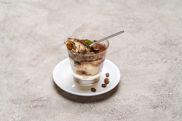 Portion of Classic tiramisu dessert in a glass cup on concrete background