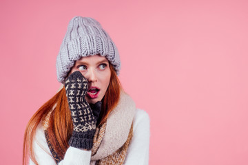 amazed redhaired ginger woman wearing stylish hat ,knitted mittens and sweater gossiping in studio pink background