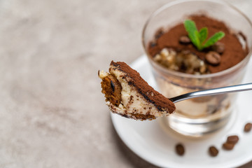 Portion of Classic tiramisu dessert in a glass cup on concrete background