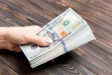 Perspective view of female hand giving one hundred dollar bills on wooden background. Charity and donation concept with copy space