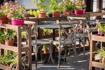 Wooden table and chairs in rustic style at an outdoor cafe with flowers in the pots as decor. Sunny day in a city street cafe