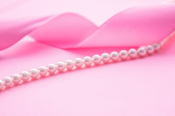 Pearl necklace and pink ribbon on pink background