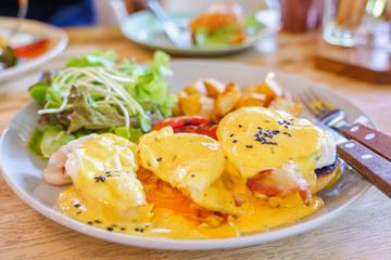 Close up egg benedict with organic salad and fried potato on with dish on wooden table background. delicious breakfast in morning..