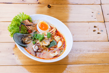 Traditional Thai food spicy soup with shrimp or tom yum seafood noodle in bow on wooden table with copy space.